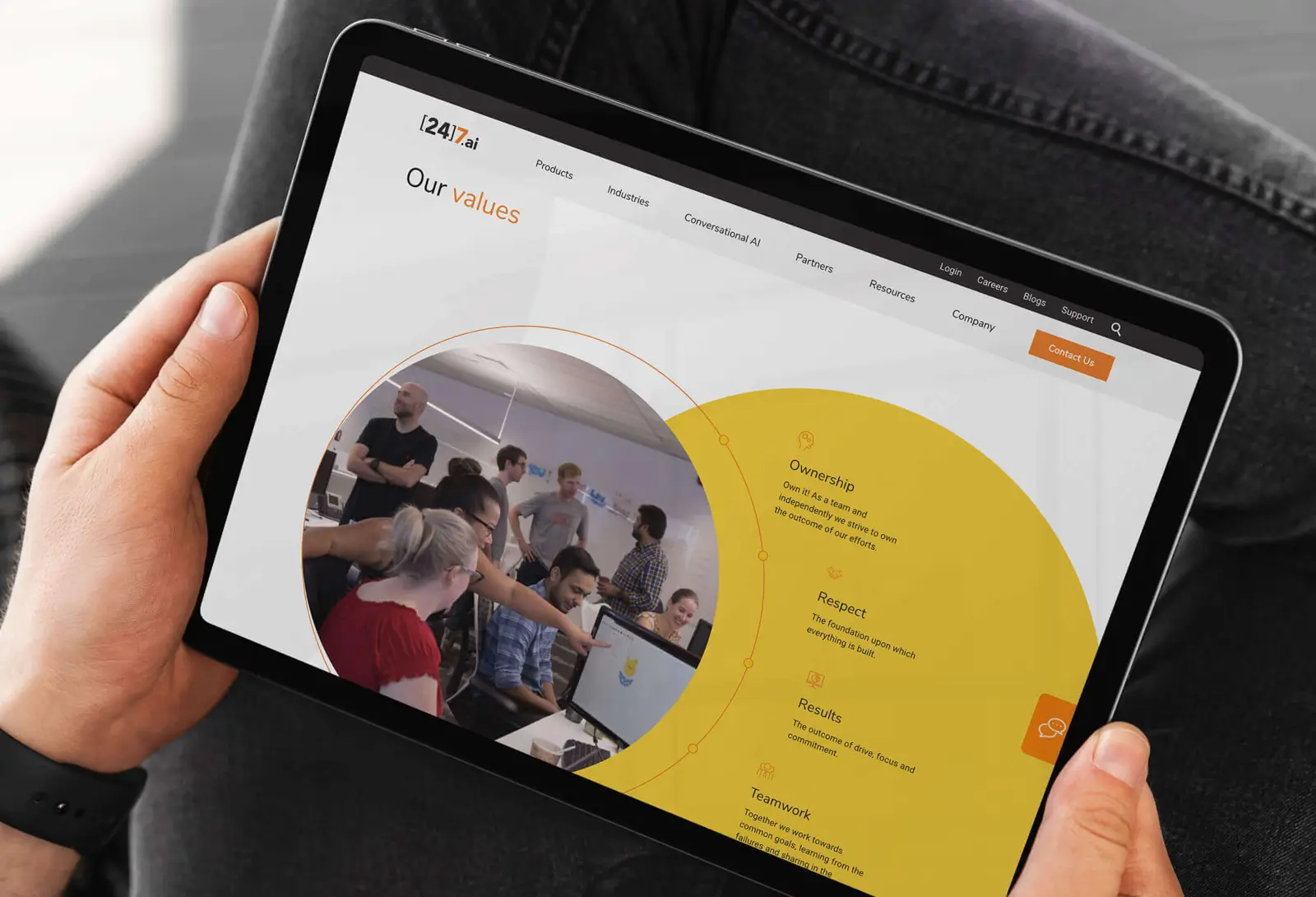 Person holding tablet showing 24.ai “Our values” page with team photo and yellow values graphic.
