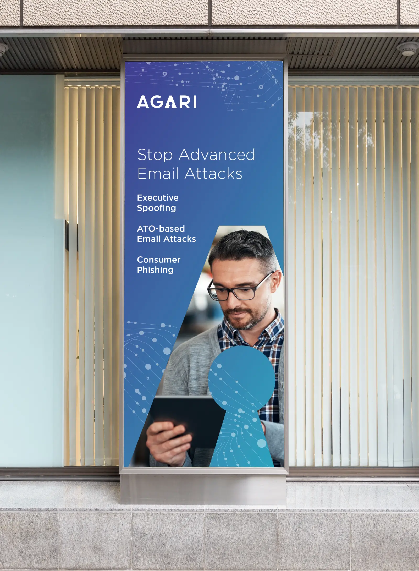 Tall Agari poster on glass window promoting protection from advanced email attacks with man using tablet.