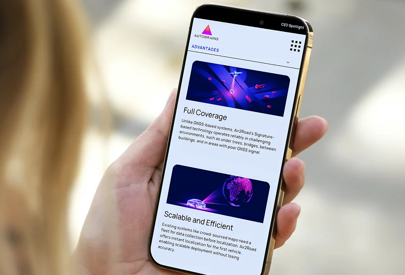 Person holding a smartphone outdoors showing the Autobrains advantages page with AI driving visuals.