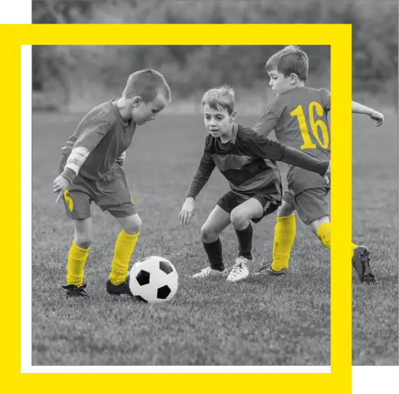 Black-and-white photo of children playing soccer with yellow uniforms and a bold yellow frame around the image.