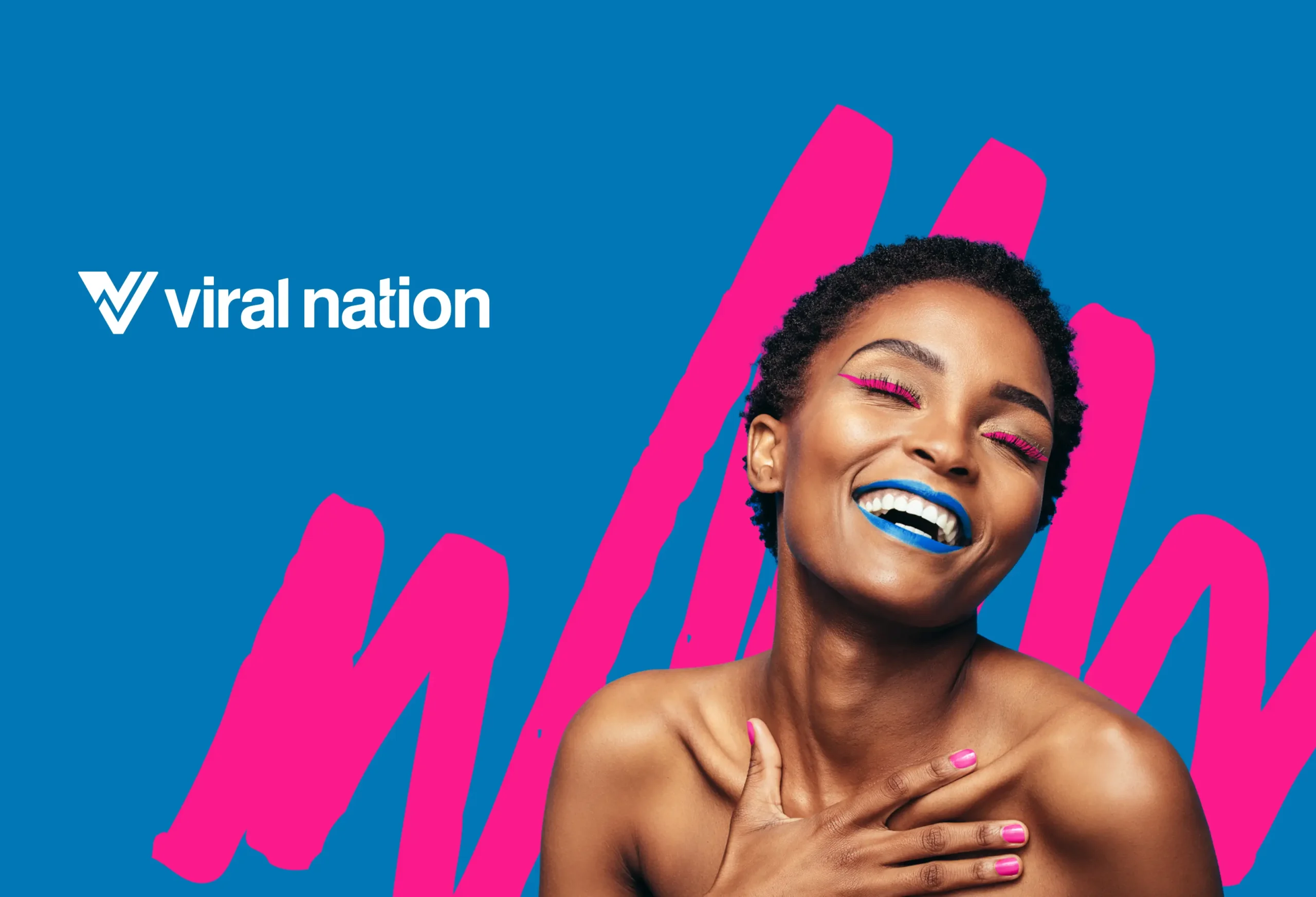 Smiling woman with bold blue lipstick and pink eye makeup in front of a bright Viral Nation brand background