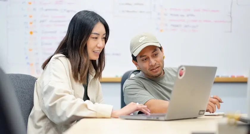 Two B2B marketing professionals reviewing AI strategy and website performance on a laptop in a collaborative office setting