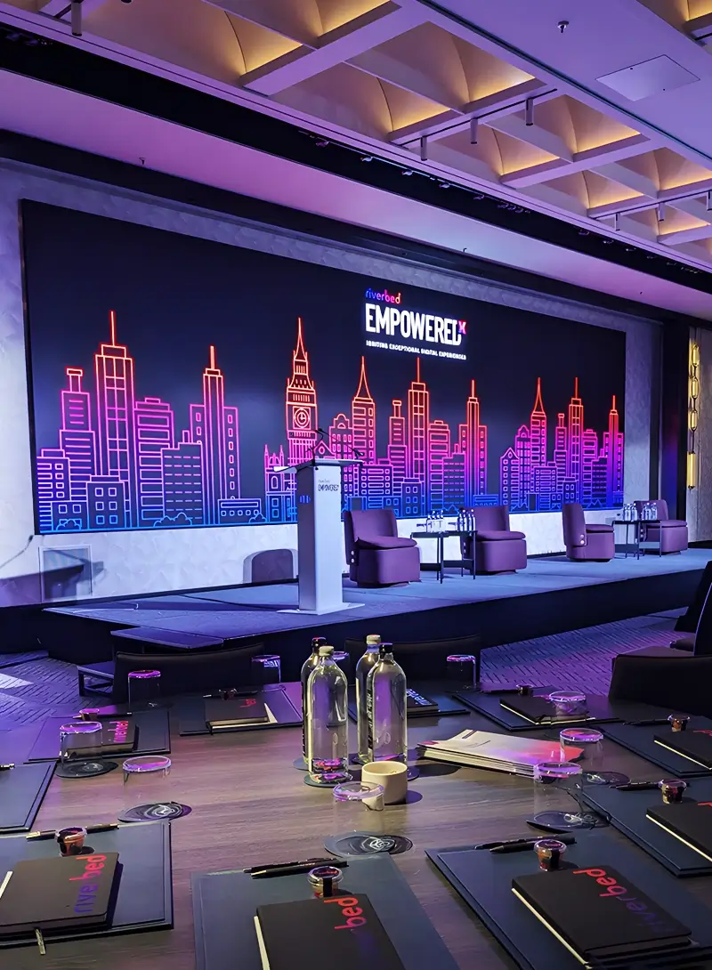 Conference stage setup with neon cityscape backdrop, podium, and seating for a corporate event.