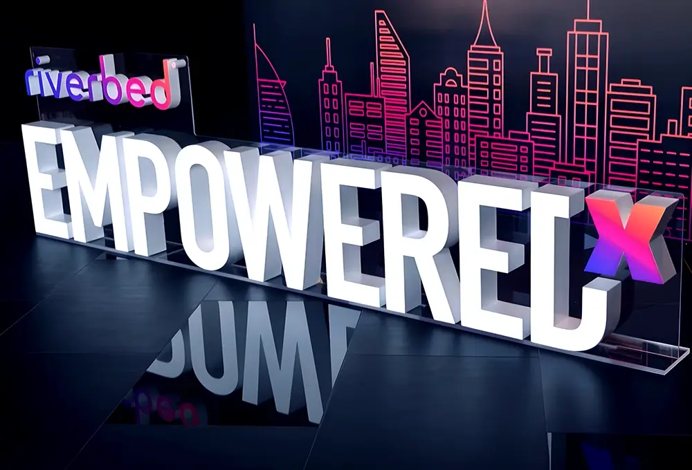 Large “EmpowerEX” event signage with Riverbed branding against a neon city skyline backdrop.