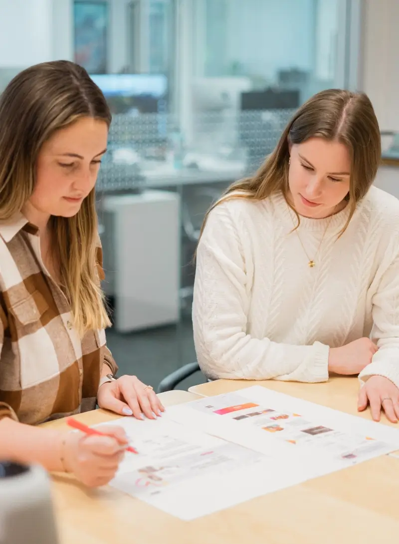 Two colleagues reviewing printed design layouts together at a desk in an office setting.