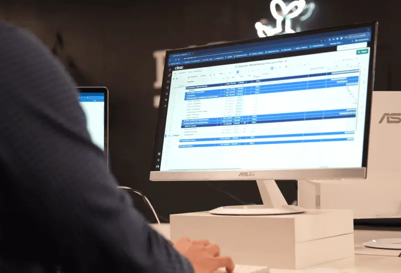 Person working at a desktop computer displaying a data management dashboard and spreadsheet-style interface in a modern workspace.