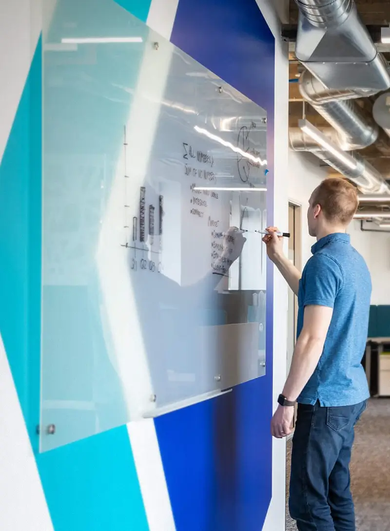 Team member writing on a glass whiteboard in a modern office workspace