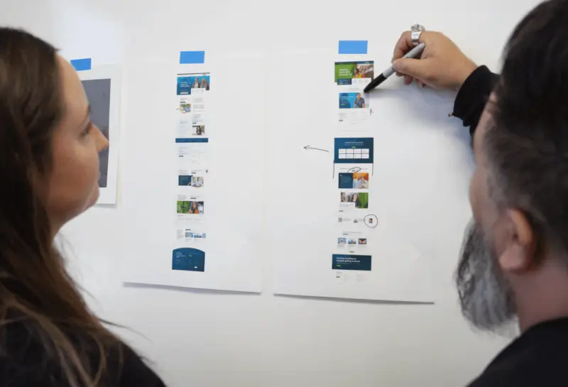 Team members reviewing and discussing printed website wireframes and UI layouts during a design planning session.