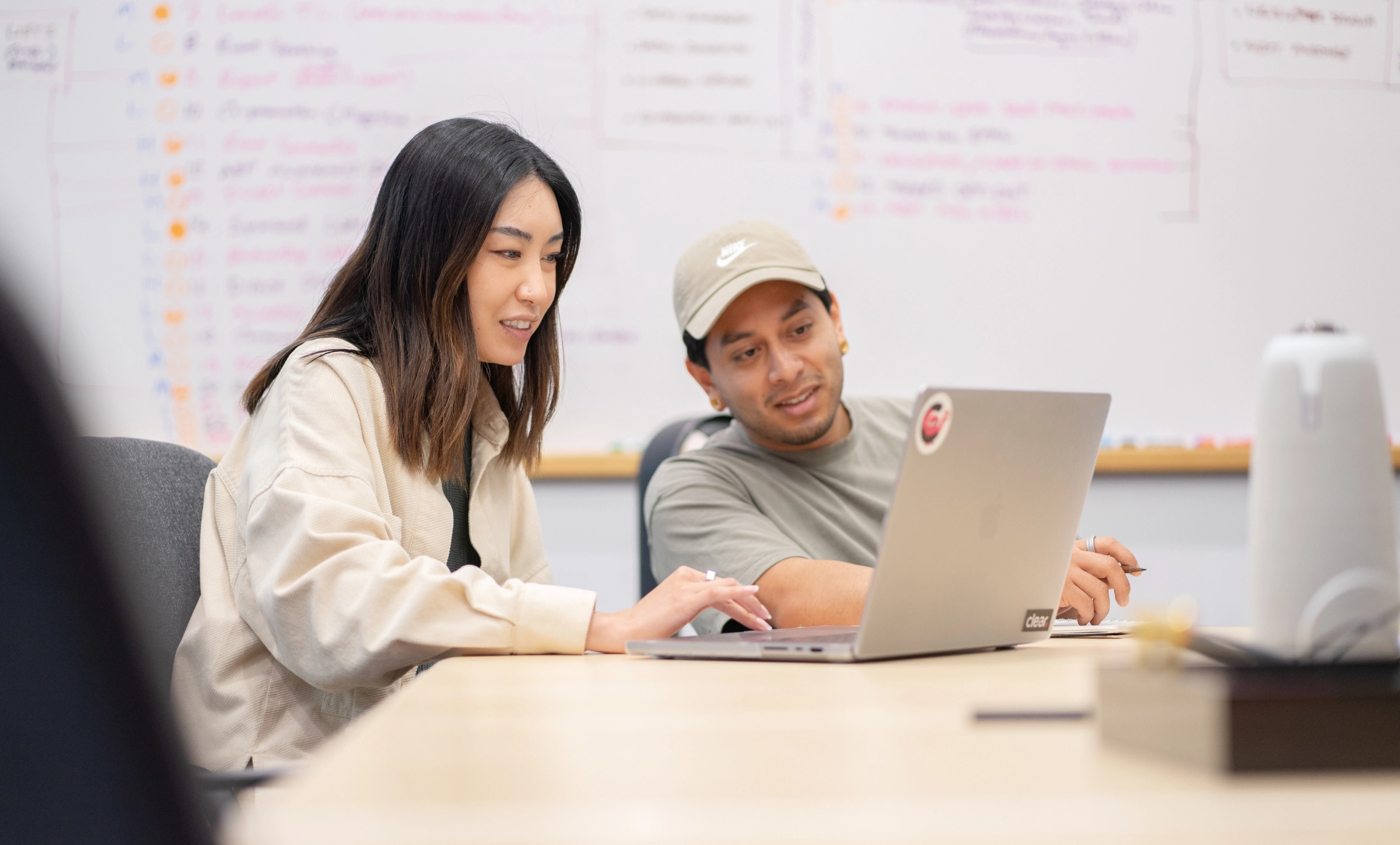 Two Clear Digital team members reviewing work together on a laptop in front of a whiteboard